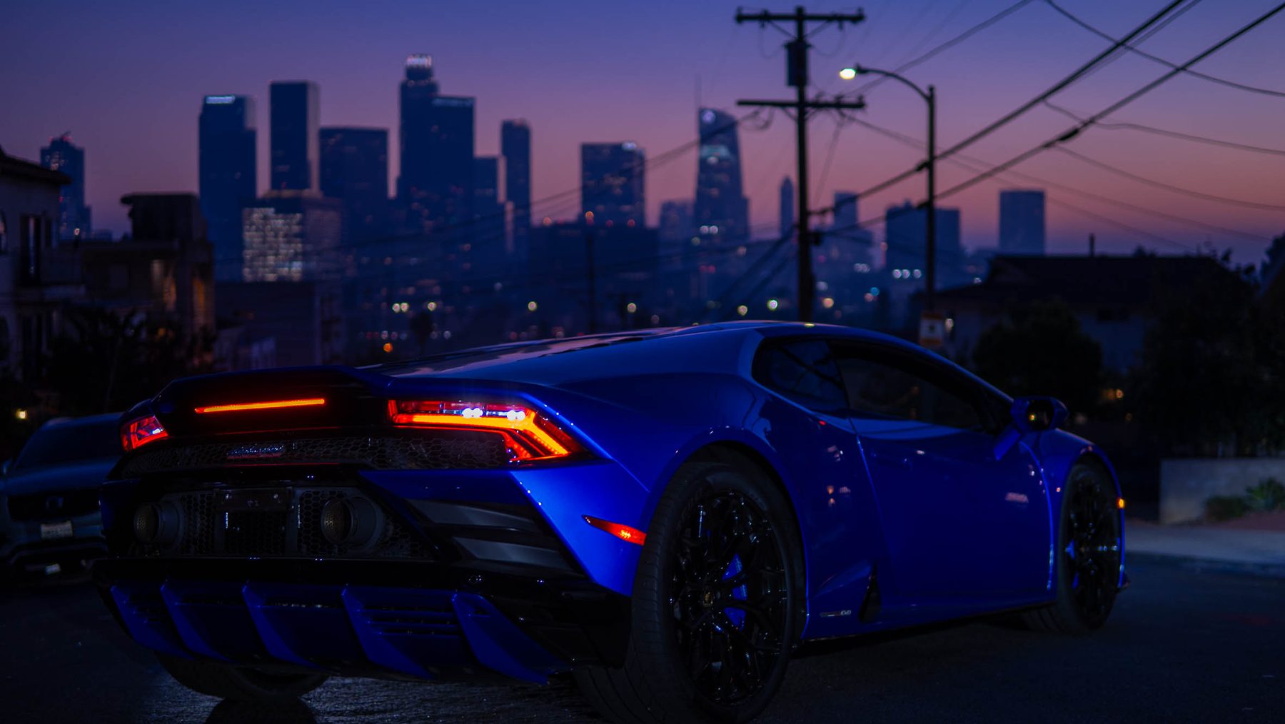Blue Lamborghini from behind with the downtown skyline at twilight
