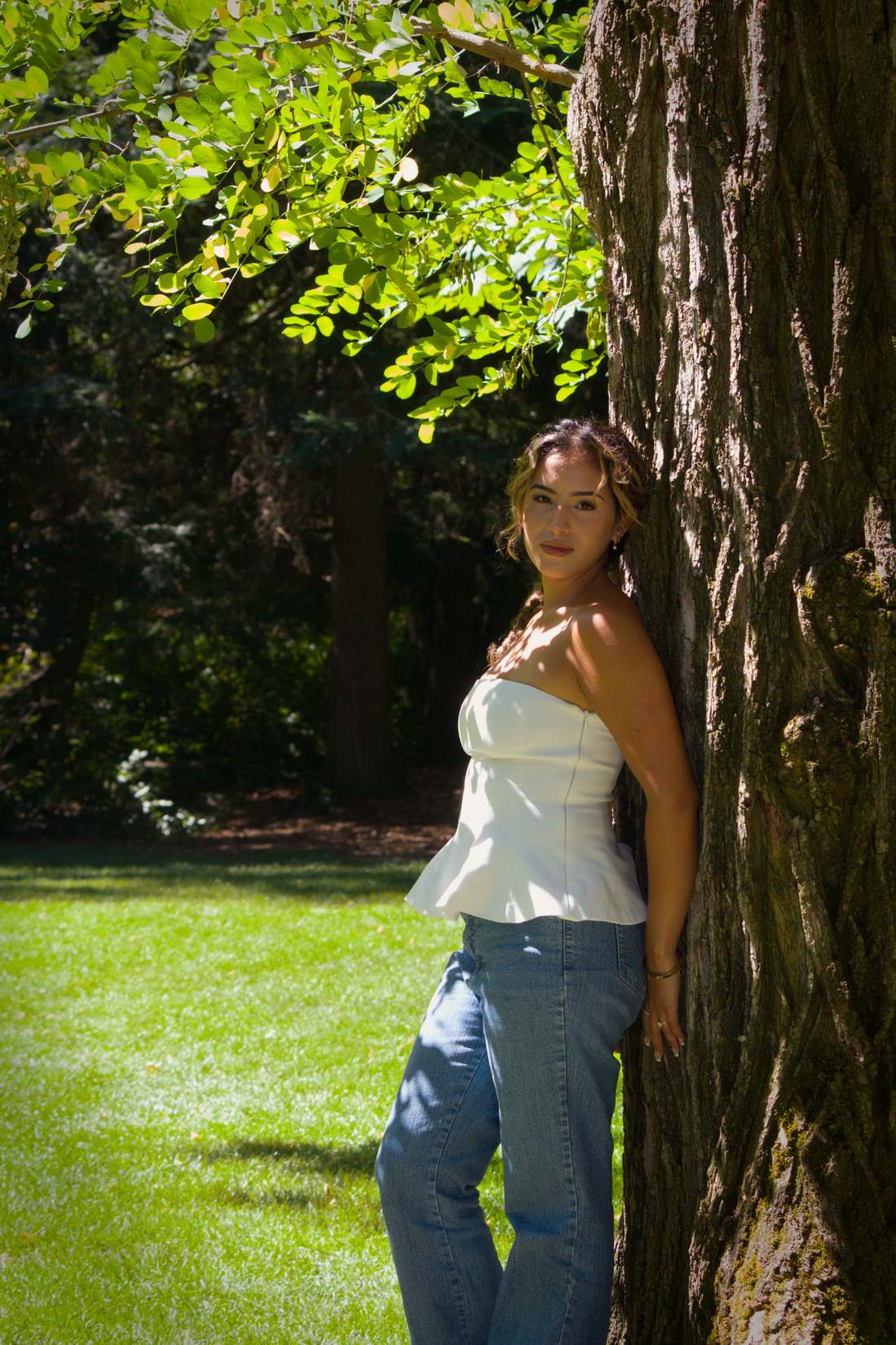 Woman in a white top leaning on a tree trunk in the sun
