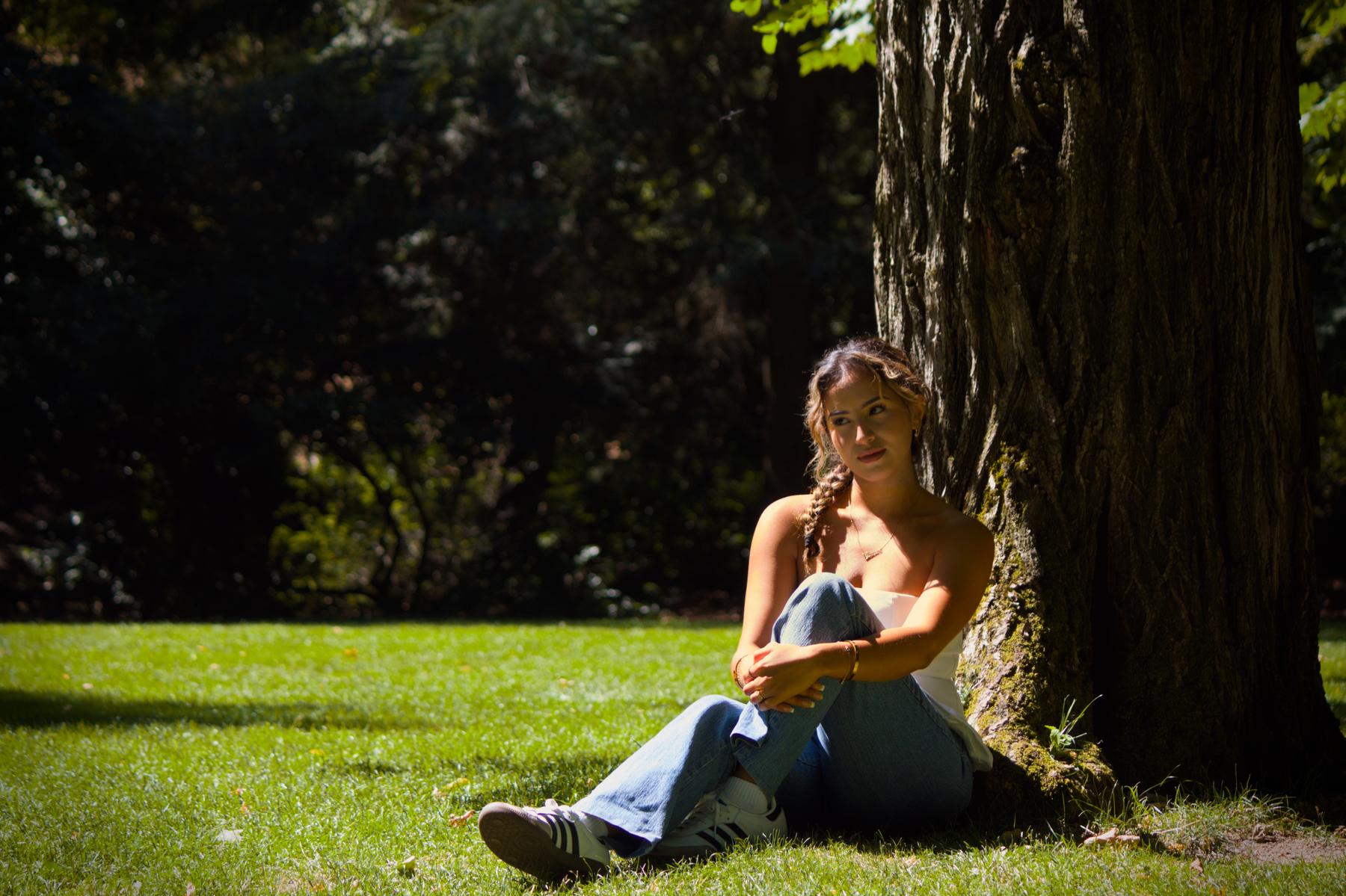 Woman sitting against a tree on the grass