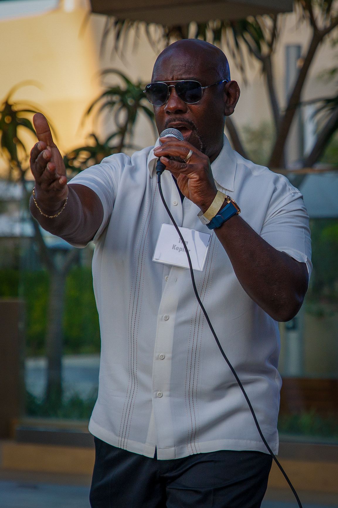 Speaker in dark sunglasses addressing the crowd with a microphone