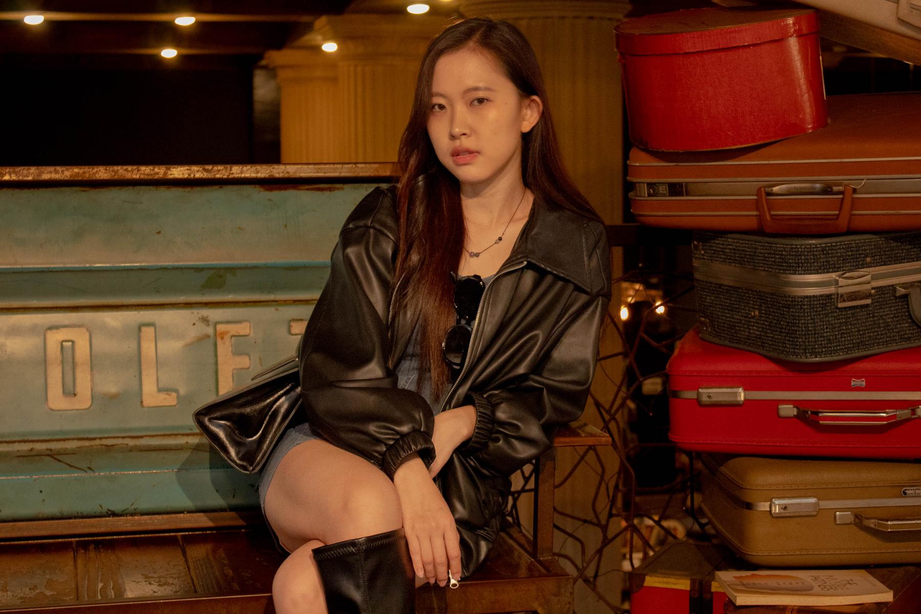 Woman in a leather jacket seated by vintage suitcases