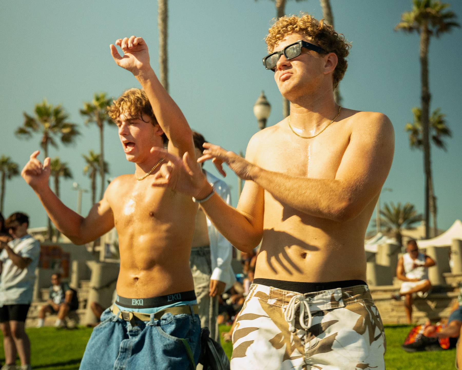 Two shirtless dancers with their arms up on the lawn at golden hour