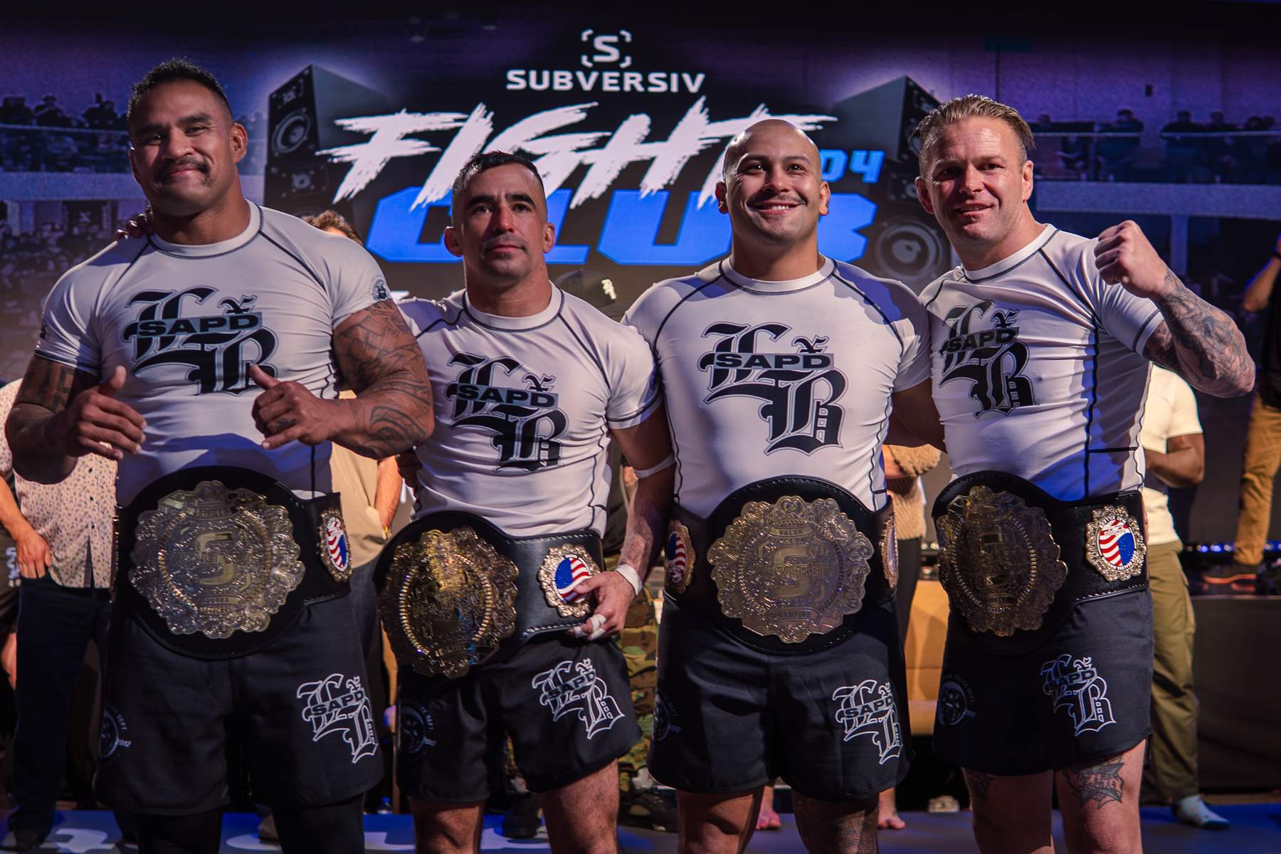 Four champions holding their belts on stage